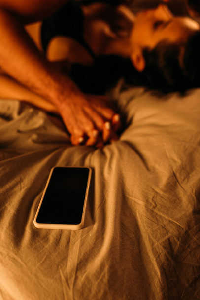 Selective focus of couple with clenched hands lying near smartphone on bed in bedroom - Foto, imagen