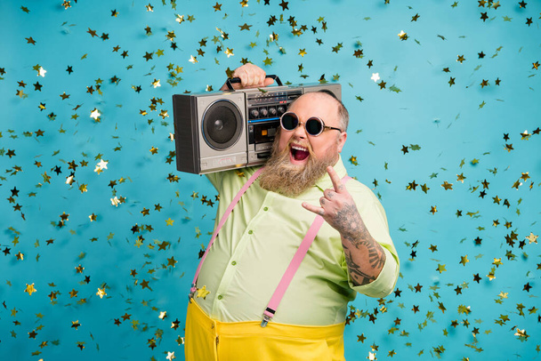 Portrait of his he nice attractive cheerful cheery funky cool crazy bearded guy carrying boombox showing horn sign isolated over bright vivid shine vibrant blue color background - 写真・画像