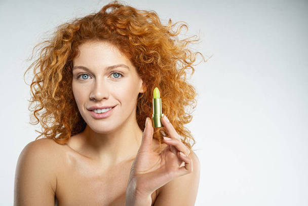 Smiling curly red female with moisturizing lipstick - Photo, image