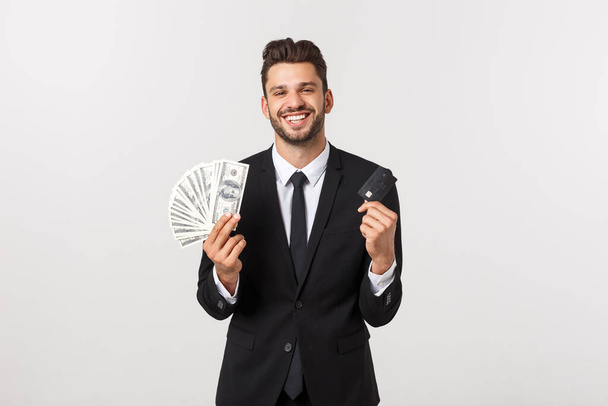 Πορτρέτο ενός χαρούμενου χαμογελαστού άνδρα που κρατάει ένα μάτσο χαρτονομίσματα και δείχνει την πιστωτική του κάρτα απομονωμένη σε λευκό φόντο. - Φωτογραφία, εικόνα