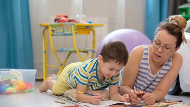 子供たちの部屋の床には幸せな母親と小さな息子が横たわっていて、一緒に絵を描いています。 - 映像、動画