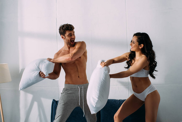 Excited boyfriend and girlfriend fighting with pillows on bed in bedroom - Foto, Bild