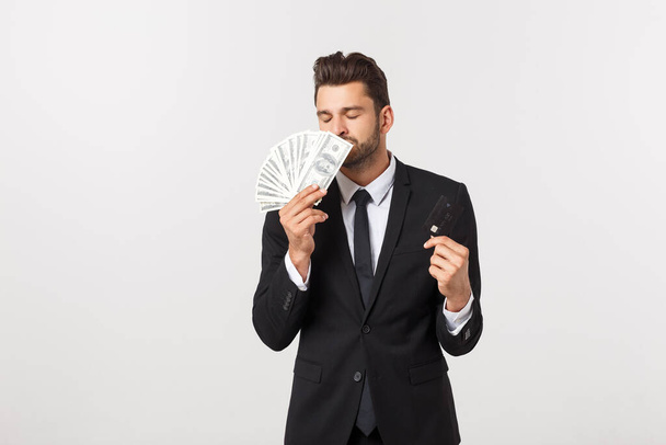 Portrait d'un homme souriant heureux tenant un tas de billets d'argent et montrant la carte de crédit isolé sur fond blanc
. - Photo, image