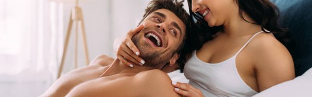 Mulher sorrindo e abraçando homem animado no quarto, tiro panorâmico
 - Foto, Imagem