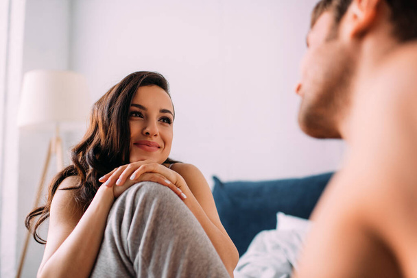 Selective focus of beautiful woman leaning on male knee and looking at boyfriend in bedroom - Fotoğraf, Görsel
