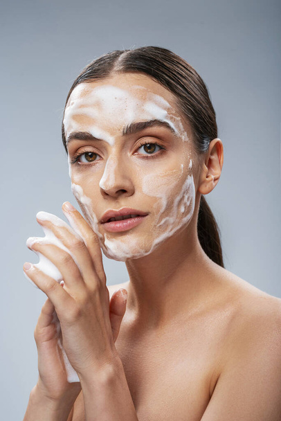 Serene young woman standing with foam on face - Foto, Imagem