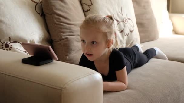 距離学習、子供のためのオンライン教育。スマホの前の家で勉強している女の子。子供はオンライン漫画、子供のコンピュータ中毒、親の制御を見ている。自宅での隔離 - 映像、動画