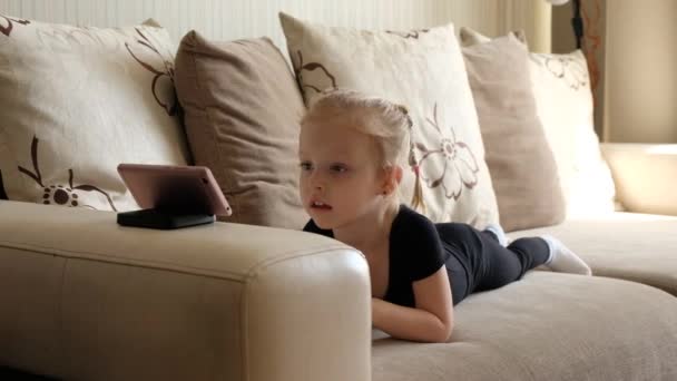 Distance learning, online education for kids. Little girl studying at home in front of the smartphone. Child watching online cartoons, kids computer addiction, parental control. Quarantine at home - Кадры, видео