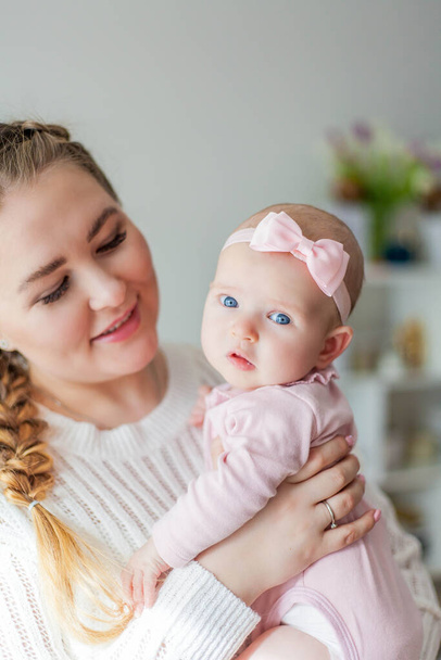 Egy gyönyörű fiatal anya karjaiban tart egy kis kék szemű, kéthónapos kislányt. Újszülött. - Fotó, kép