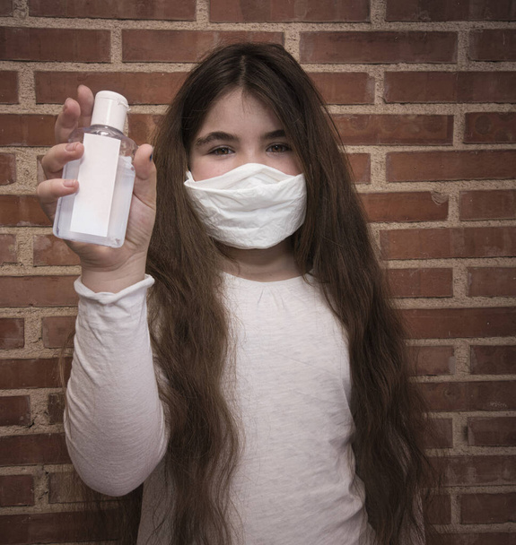 Ein Mädchen mit Maske und Händedesinfektionsmittel vor einer Wand - Foto, Bild