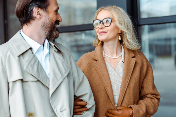 Smiling businesswoman looking at handsome businessman near building on urban street  - Photo, Image