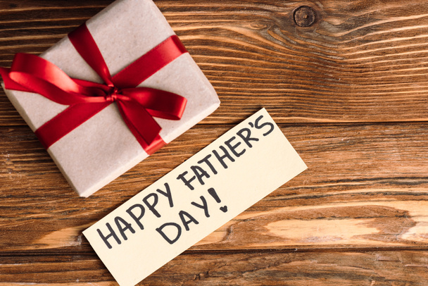Vista superior de la tarjeta de felicitación con letras feliz día de los padres y caja de regalo rosa con lazo rojo sobre fondo de madera
 - Foto, imagen