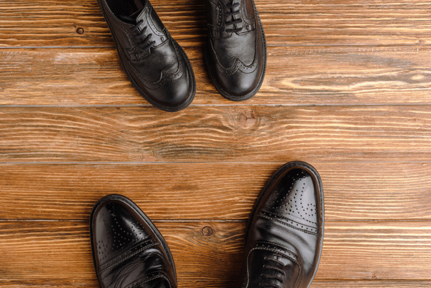 Vue du dessus des chaussures classiques noires pour hommes et enfants sur fond en bois, concept de fête des pères
 - Photo, image