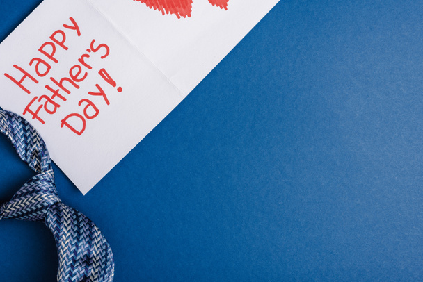 Vista superior de la corbata para hombre y tarjeta de felicitación con letras feliz día de los padres sobre fondo azul
 - Foto, imagen