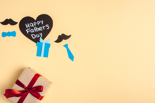 vista superior de la caja de regalo, elementos decorativos de papel y tarjeta en forma de corazón de saludo con letras feliz día de los padres sobre fondo beige
 - Foto, imagen
