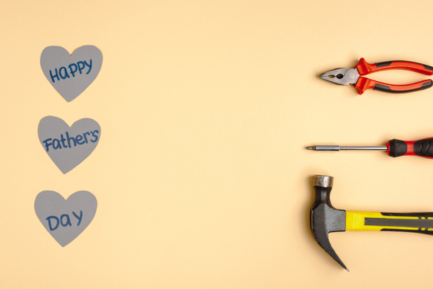 Flache Lage mit Hammer, Schraubenzieher, Zange und Papierherzen mit Schriftzug Happy Vatertag auf beigem Hintergrund  - Foto, Bild
