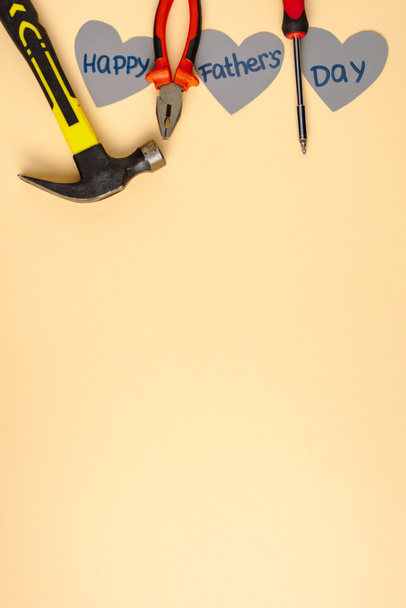 top view of hammer, screwdriver, pliers and grey paper hearts with lettering happy fathers day on beige background  - 写真・画像