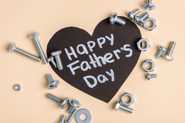 Top view of metal nuts and bolts and black greeting card with lettering happy fathers day on beige background  - Zdjęcie, obraz