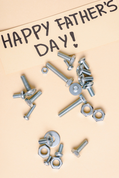 top view of metal nuts and bolts and beige greeting card with lettering happy fathers day on beige background  - Foto, Imagen