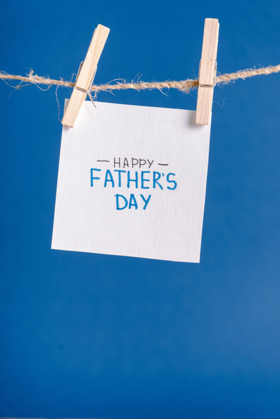 White paper with handwritten lettering happy fathers day hanging on rope with clothespins isolated on blue - Foto, Imagen