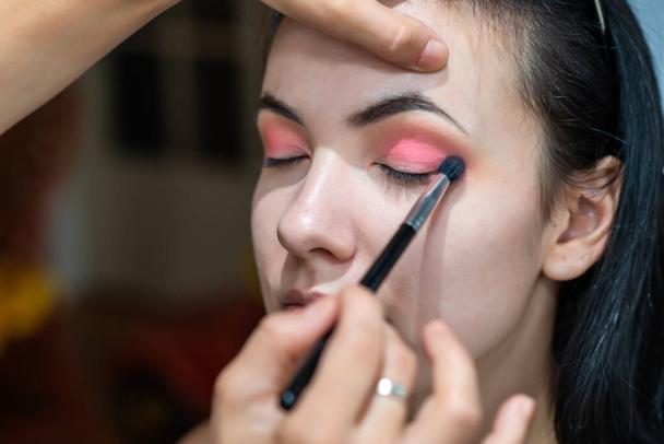 Make-up malíř nanáší oční stíny na krásnou dívku. Make-up umělec dělá profesionální make-up krásné mladé ženy.  - Fotografie, Obrázek