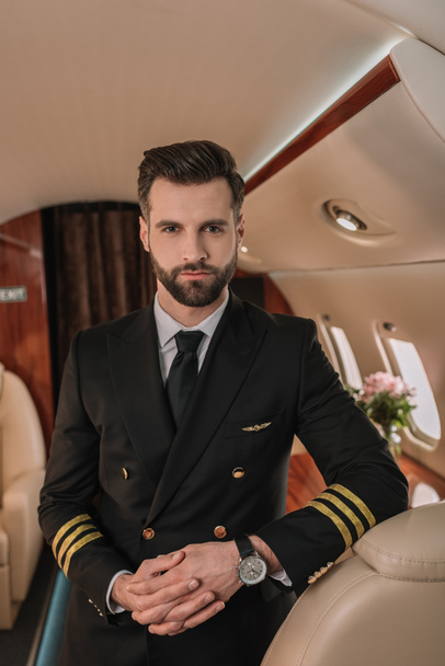 handsome, confident pilot looking at camera while standing in plane - Φωτογραφία, εικόνα
