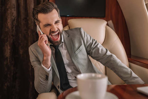 hombre de negocios enojado gritando en el teléfono inteligente mientras vuela en jet privado
 - Foto, Imagen