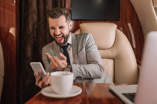agresivo hombre de negocios mostrando enredo dedo mientras tiene chat de vídeo en el teléfono inteligente
 - Foto, Imagen