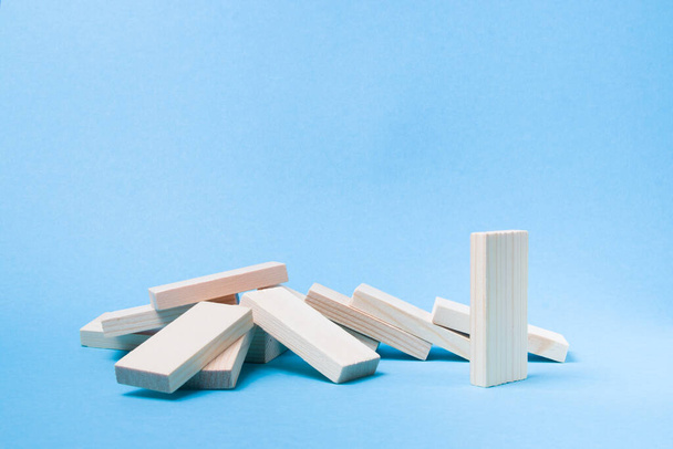 several wooden dominoes fell, one domino remained standing, maintaining social distance is important during a pandemic, stop coronavirus concept, blue background, copy location - Foto, imagen