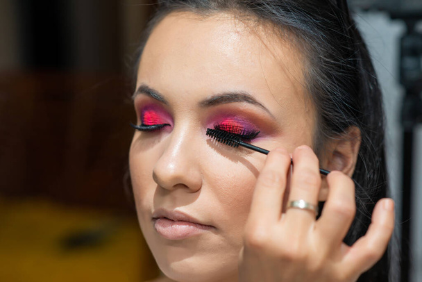 Woman applying black mascara on eyelashes with makeup brush. Make up artist doing professional make up of beautiful young woman.  - Foto, Imagen