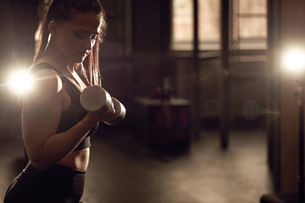 Candid strong young woman is training with a dumbbells in the gym. Real wokout - Photo, Image