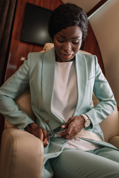 atractiva mujer de negocios afroamericana abrochando cinturón de seguridad en jet privado
 - Foto, Imagen