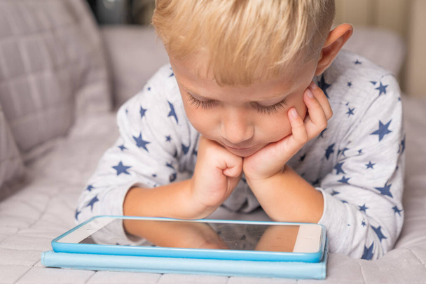 Caucasian child boy using digital tablet while lying on sofa at home - Foto, imagen