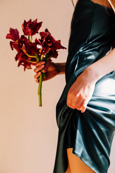 Ellerinde kırmızı çiçekler olan ve bacağını kaldıran yeşil ipek bir elbise giyen bir kız. - Fotoğraf, Görsel