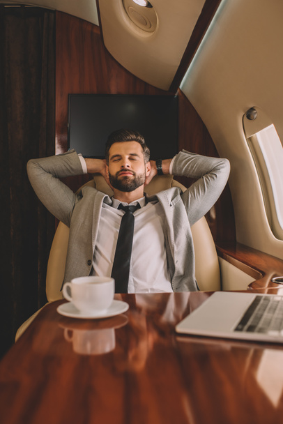 jonge zakenman rusten met de handen achter het hoofd en gesloten ogen in prive jet - Foto, afbeelding