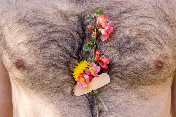 Kleine Bouquet Frühlingsblumen auf dem Körper erwachsenen bärtigen Mann geklebt. Das Konzept Frühlingszeit nach der Pandemie. - Foto, Bild