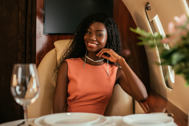 selective focus of elegant african american woman smiling at camera in private plane - Fotoğraf, Görsel