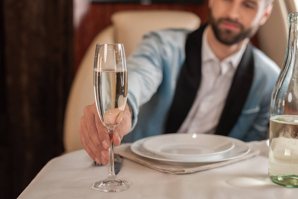 selective focus of elegant man taking glass of champagne from served table in private plane - Foto, imagen