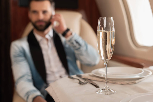 selective focus of elegant man talking on smartphone near glass of champagne in private jet - Foto, Imagen
