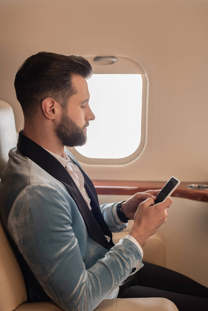 vista laterale di elegante giovane uomo messaggistica su smartphone in aereo privato
 - Foto, immagini