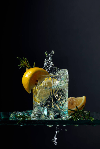 Boisson gazeuse avec glaçons, citron et romarin sur une table en verre. Fond noir, espace de copie
. - Photo, image