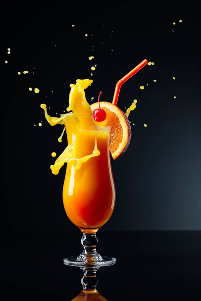 Orange juice and cherry on a black reflective background. - Foto, afbeelding