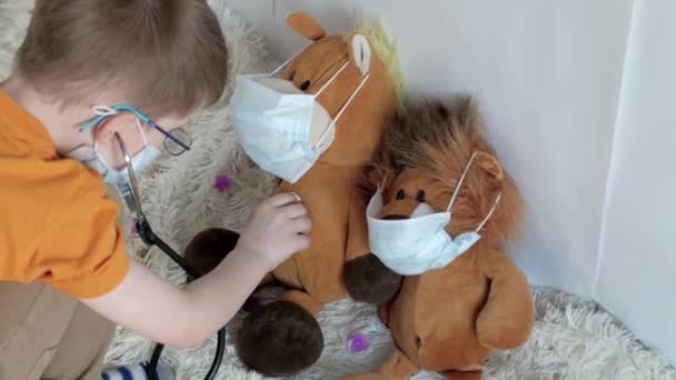 in a bright room, a boy with blue eyes in a medical mask, with, a yellow t-shirt listening, to brown toys horses, and hedgehogs, in a close-up stethoscope, on sitting on the floor. - Filmagem, Vídeo