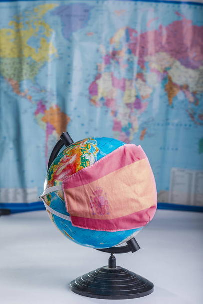 Globe σε μια ιατρική μάσκα με την εικόνα της σημαίας της Ισπανίας. Πανδημική έννοια - Φωτογραφία, εικόνα