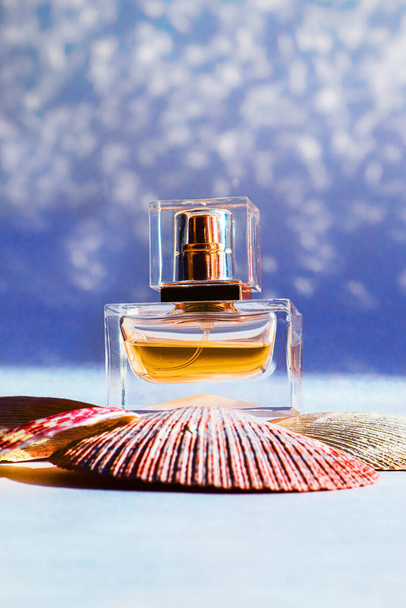 Glass bottle of fragrant perfume is on the sea shells on blue background - Photo, image