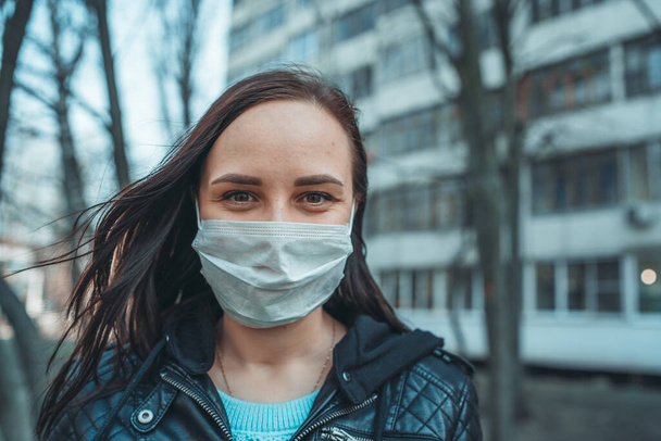 Portrait of young woman in medical mask on her face standing on street. Adult female covered her face with mask to protect yourself from diseases. - Фото, зображення