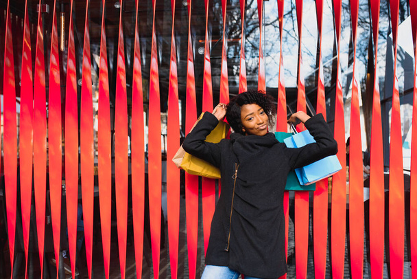 Portrait of beautiful young black woman smiling with shopping bags outside - Foto, afbeelding