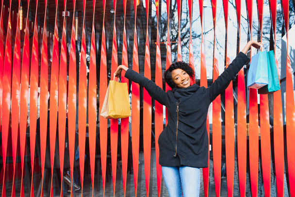 Portrait of beautiful young black woman smiling with shopping bags outside - Zdjęcie, obraz