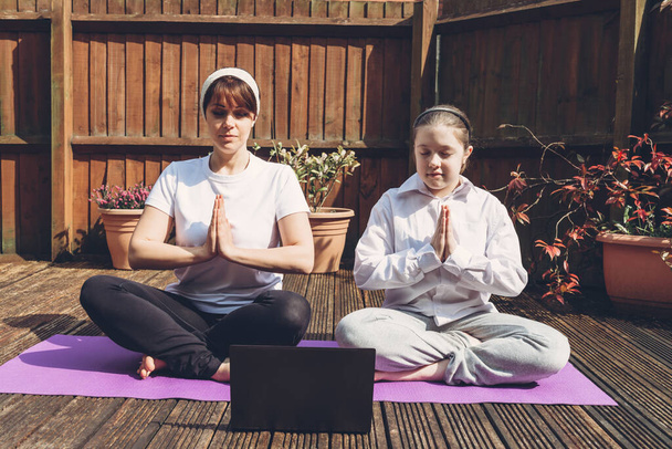 Boldog anya és lánya csinálnak online jóga laptop alatt elszigeteltség a hátsó kertben, nincs felszerelés edzés, meditációs tippek kezdőknek, maradj otthon, és maradj egészséges koncepció - Fotó, kép