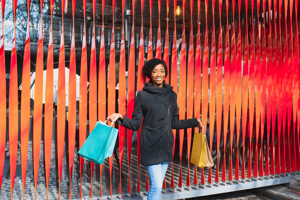 Attraktive junge Afroamerikanerin beim Einkaufen - Einkaufstüten, Outdoor, Straßenblick, geeignet unter anderem für Weihnachtseinkäufe - Foto, Bild